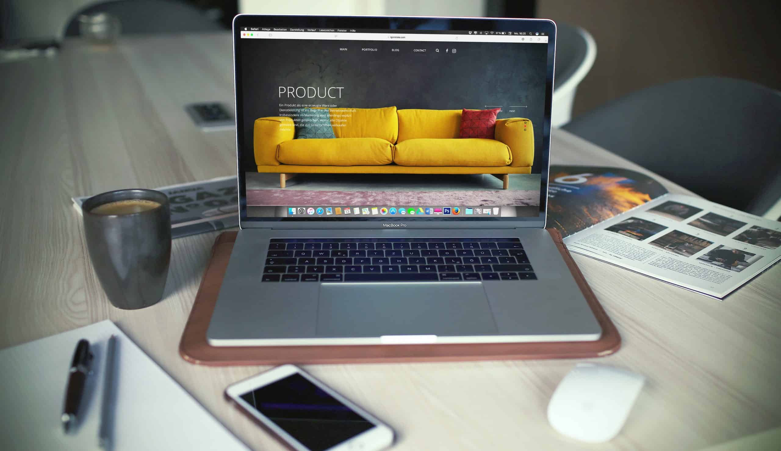Bild vom Arbeitstisch aus dem Büro. Zu sehen ist ein Macbook mit einer Kundenwebseite geöffnet