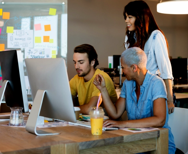 Drei Personen arbeiten gemeinsam an einem Computer in einem modernen Büro